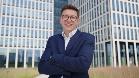 a young happy businessman looks and smiles at the camera in front of an office building