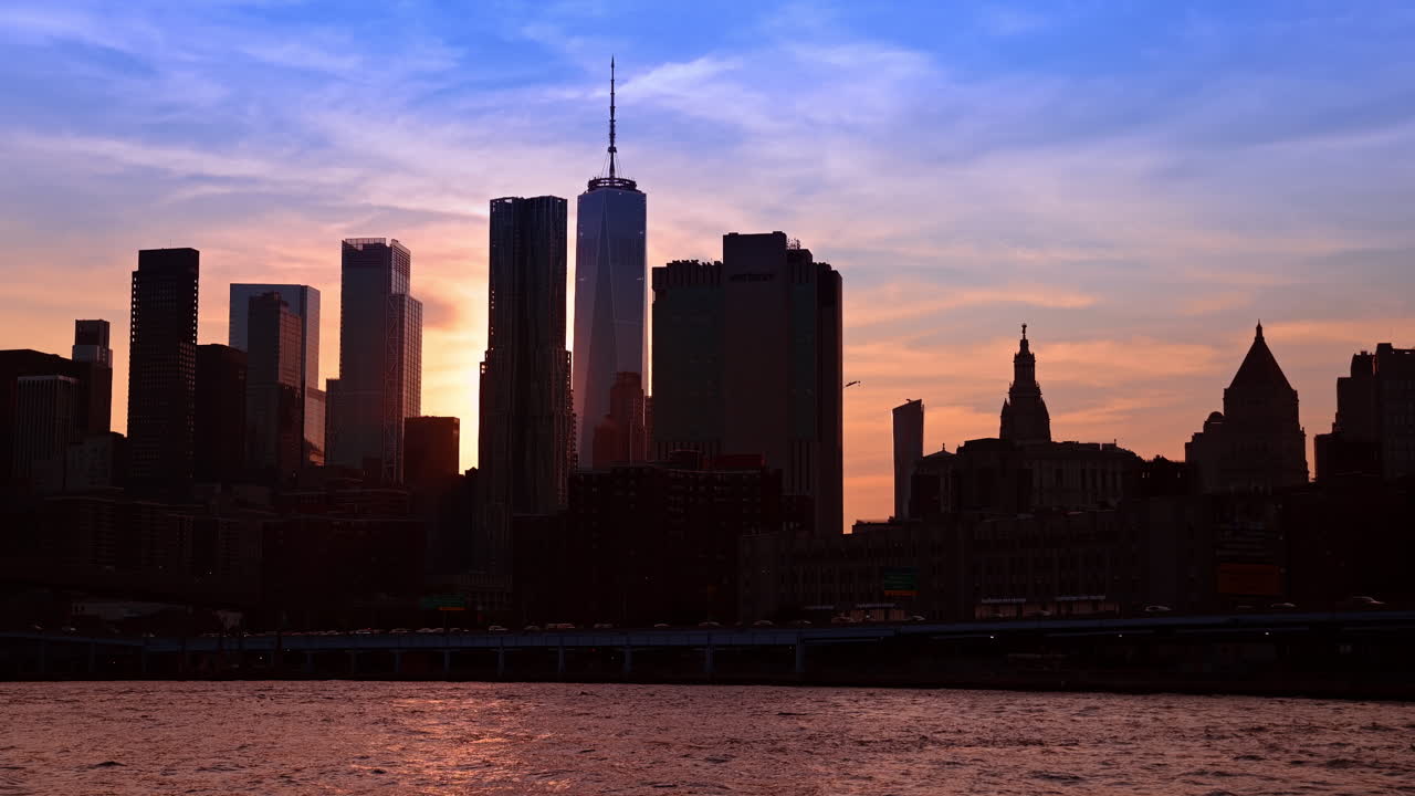 Nueva York, EE. UU., 9 de agosto de 2025: Silueta al atardecer del horizonte de Manhattan y el One World Trade. Silueta oscura de los rascacielos del distrito financiero de Lower Manhattan contra un cielo al atardecer vibrante de color naranja y azul.