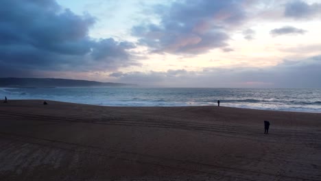 vuelo aéreo sobre la playa de nazare durante la luz de la tarde con la silueta de la gente mirando al mar