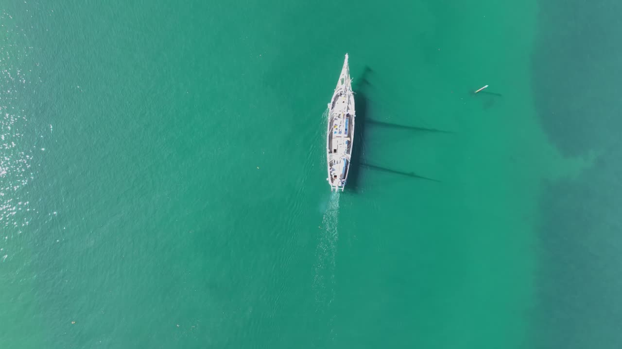 Overhead drone clip of a wooden ship salling through clear green seawater