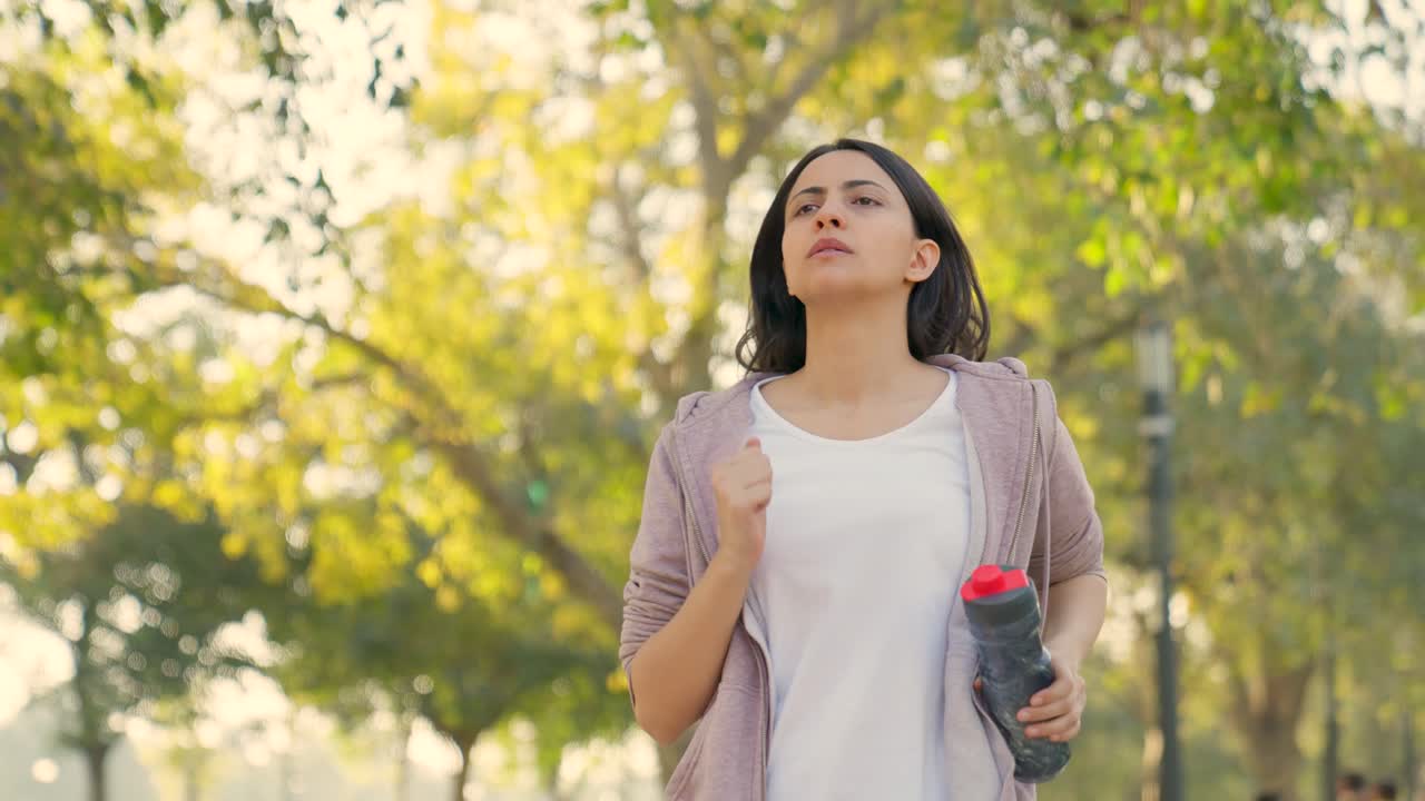 mujer corriendo con una botella de agua en un parque por la mañana