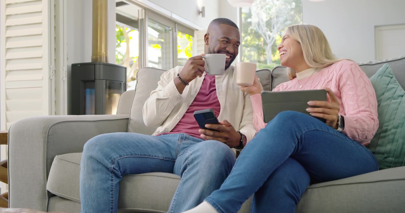 Coppia afroamericana che guarda un uomo condividere contenuti dal telefono, con la donna che ride sul divano con un tablet