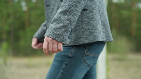 a close-up view of a man's hand and grey suit jacket sleeve, as he walks outdoors. his hand is relaxed by his side, and he is wearing blue jeans