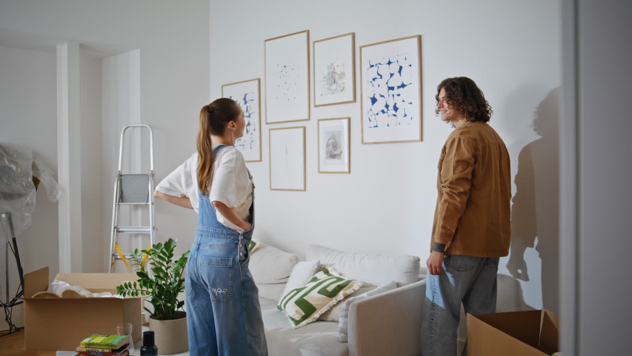 Couple hanging pictures wall apartment. Happy woman and man enjoy collaborating