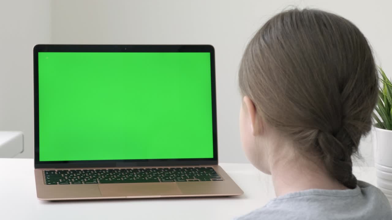 School girl studying during online lessons in front of green screen laptop, back view