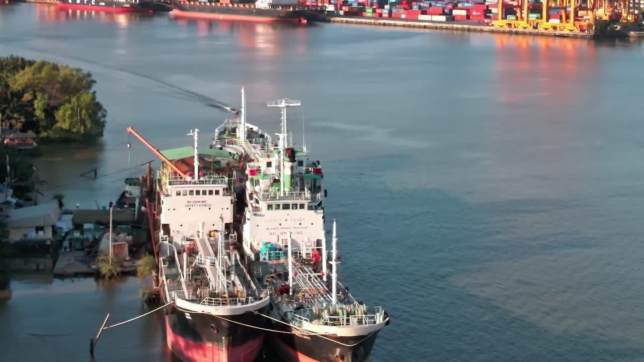 View of ships docked on river in Bangkok with city buildings in background