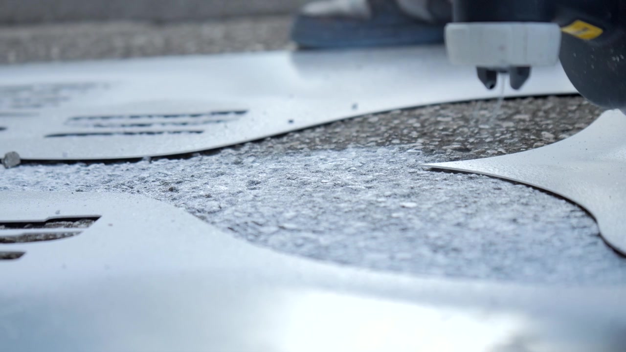 Close-up de um artista de rua pulverizando tinta através de um estêncil no pavimento, revelando um design gráfico em um processo de criação de grafite e arte de rua urbana.