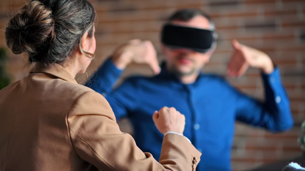 Man using a Virtual Reality headset in an office while woman explains and gesticulates