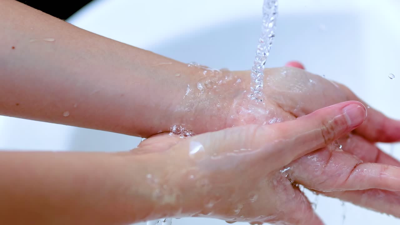 Primo piano di mani che vengono lavate accuratamente sotto un getto d'acqua, con attenzione alla tecnica e alla pulizia.