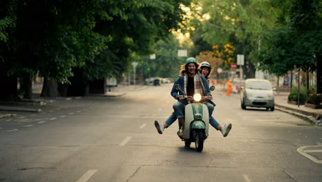 un chico feliz con el cabello largo y rizado en una chaqueta de vaqueros monta un ciclomotor en la carretera con su novia feliz y extiende las piernas en diferentes direcciones mientras monta en una concurrida calle de la ciudad de la mañana