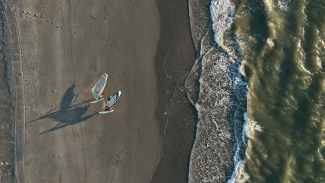 couple of windsurfer leaving north sea walking on sandy beach with kite at sunset - aerial top down