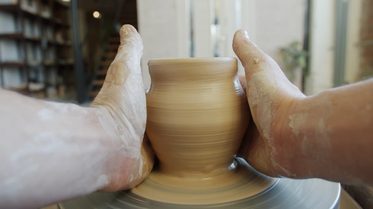 Hands shaping a clay pot on a pottery wheel