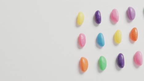 Video-of-overhead-view-of-rows-of-multi-coloured-sweets-with-copy-space-over-white-background