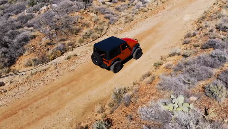 Aerial-of-Orange-Off-Road-Vehicle-Driving-on-Dirt-Road-through-Desert-Mountains---View-from-Side-of-Vehicle