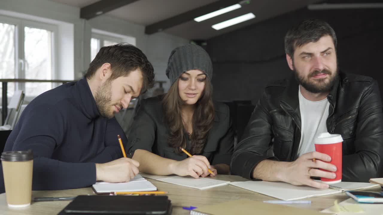 Team of young professionals having a meeting in a creative office. Taking notes and listening to the team leader. Business discussion. Coffee cups on the table. Shot in 4k