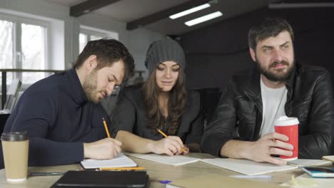 team of young professionals having a meeting in a creative office. taking notes and listening to the team leader. business discussion. coffee cups on the table. shot in 4k