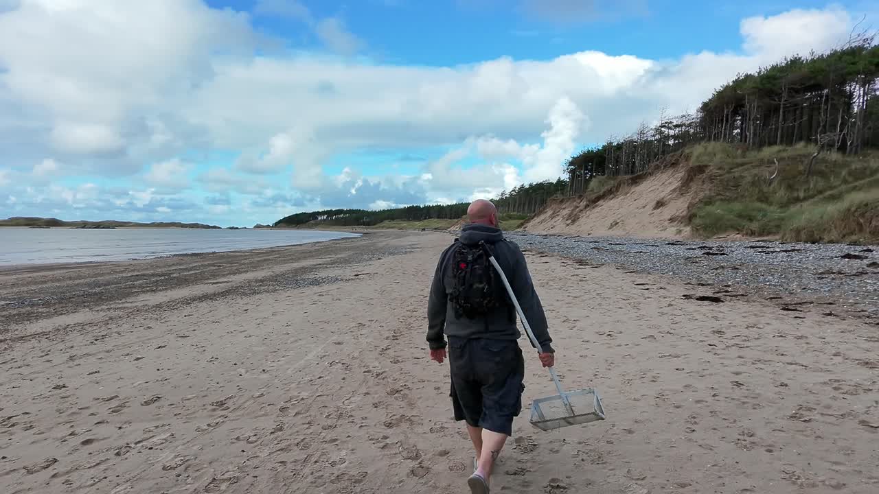 Following male with sand scoop walking dog on beautiful Welsh beach for early morning relaxation