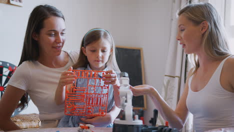 same sex female couple making robot from kit with daughter at home together