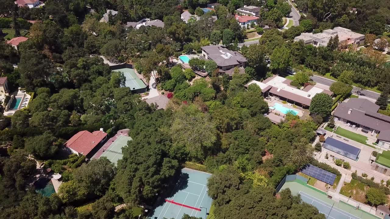 Aerial shot over an upscale Pasadena neighborhood pulls back and rises, to reveal leafy residential blocks with swimming pools and private tennis courts. Toward a broad view of the San Gabriel Valley