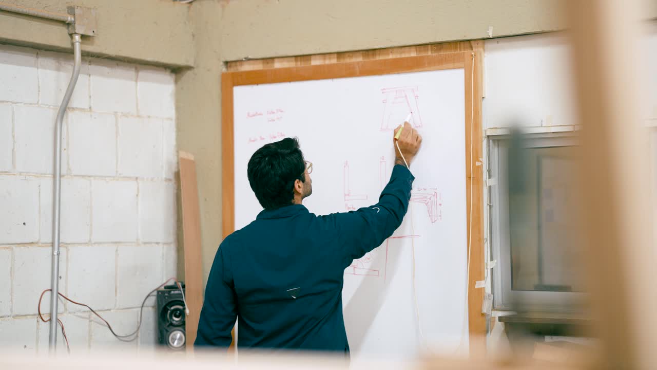 Mand tegner på whiteboard i et værksted