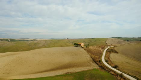 tuscany rolling fields and farmhouse by road, captured in wide landscape establishing from above