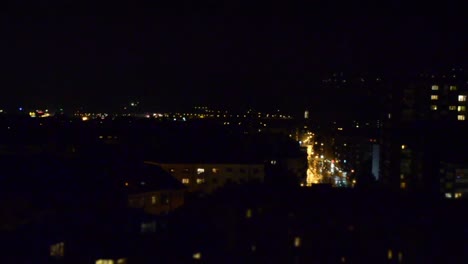 Miniature-effect-timelapse-of-a-small-city-at-night-with-a-small-street-with-cars-passing-through-and-illuminated-streets-and-houses-in-the-background