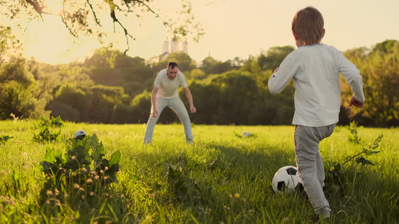 joven padre con su pequeño hijo jugando al fútbol en el campo de fútbol