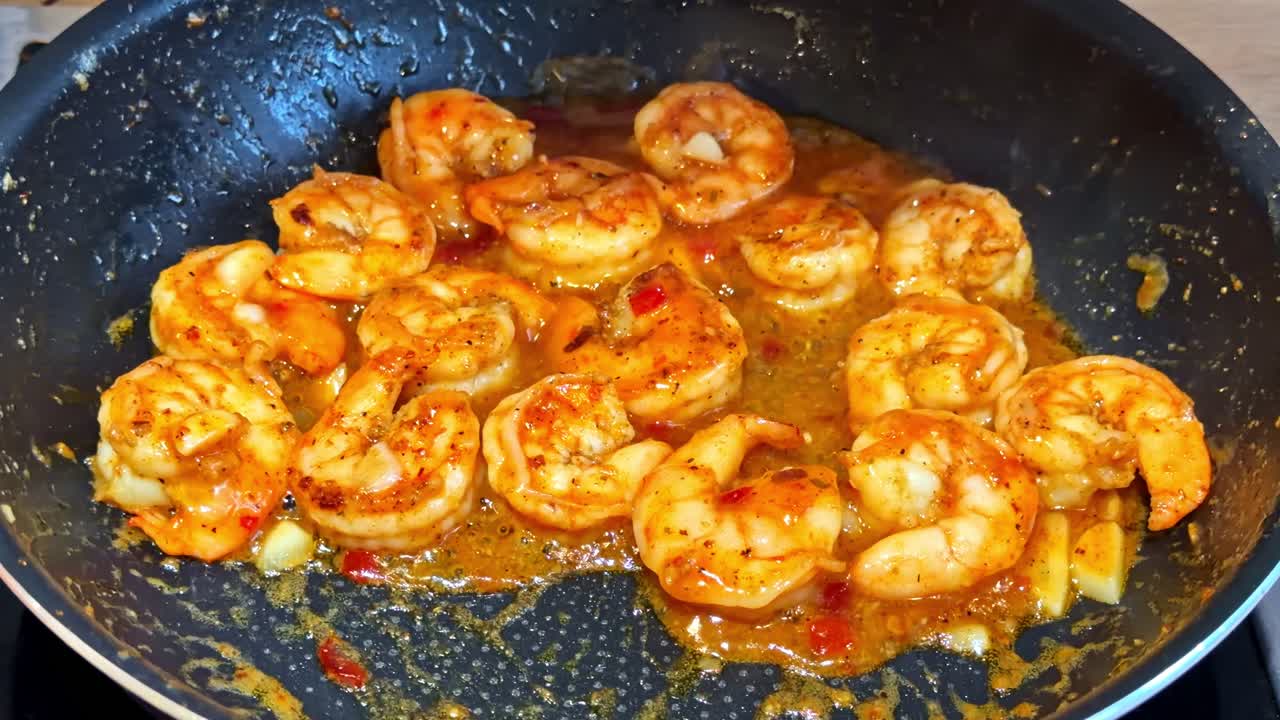 Gamberi cuociono in una salsa piccante e aromatica in una padella, rilasciando vapore e colori vivaci. Ottimo per programmi di cucina o contenuti culinari.