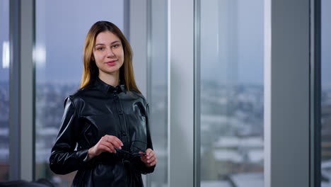 woman in a black leather jacket, looking at the city view through a window