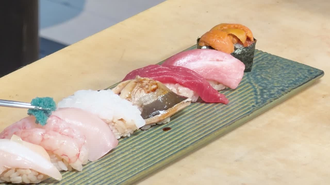 新鮮な握り寿司に、シェフが丁寧に緑色の飾りを添えているクローズアップ写真。