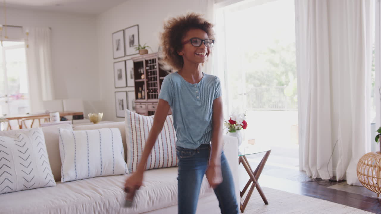 Pre-teen girl holding smartphone and dancing to music in the living room at home, close up