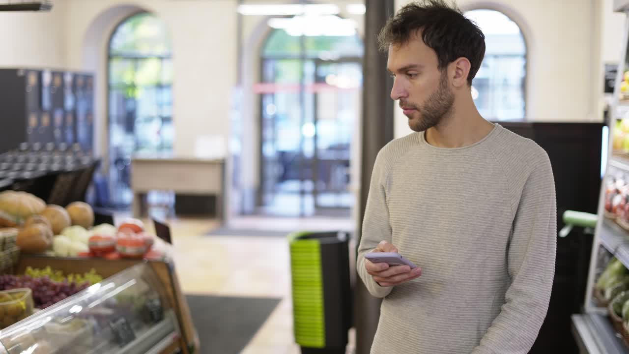 hombre relajado caminando por la tienda mirando la pantalla de su teléfono inteligente