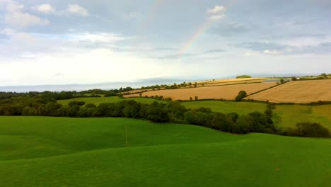 Aerial-fly-over-green-field-with-rainbow