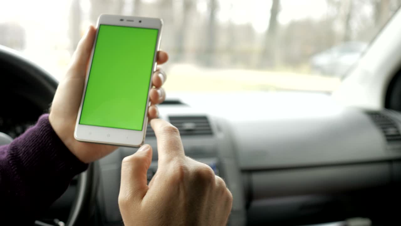 una mano sosteniendo un teléfono inteligente con pantalla verde en blanco en el coche para la dirección, masaje, ubicación, negocio. hombre se sienta en un coche moderno y trabaja en teléfono inteligente - pantalla verde - primer plano. llave de croma.