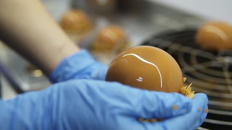 process of creating delicious dessserts. unrecognizable confectioners hands in blue gloves take cakes off tray and decorate with crisps. close-up footage