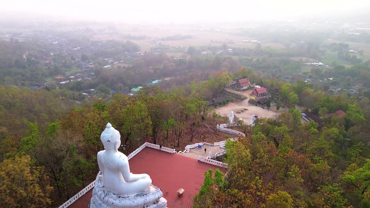 Massive seated Buddha statue on hilltop near Pai, Thailand under cloudy sky, aerial flyover dolly