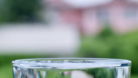 a single drop of water hitting the surface of crystal-clear water causing movement and wave in a transparent glass cup on a blurry background