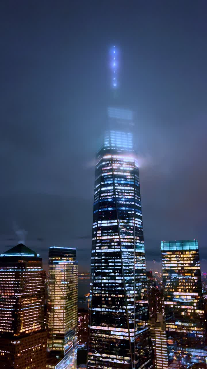 Nebbia intorno al One World Trade Center di notte. Il One World Trade Center tra le nuvole basse, skyline illuminato di notte, vista aerea verticale di Lower Manhattan.