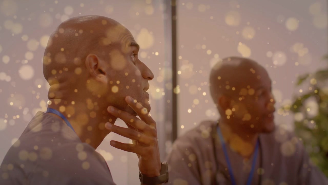 Homme principal écoutant attentivement lors d'une réunion d'affaires, un collègue gesticulant près d'un PC, avec un bokeh doré sur les sujets.