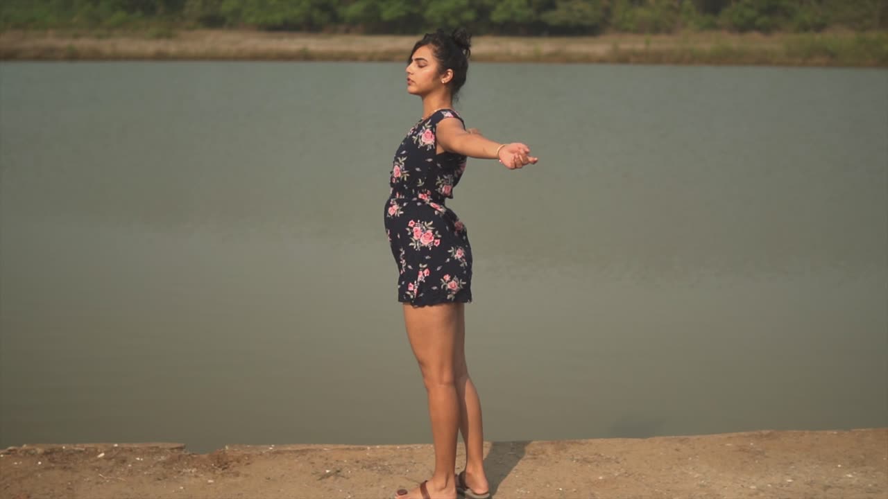 niña india con un vestido floral girando en cámara lenta con los brazos abiertos frente a un lago