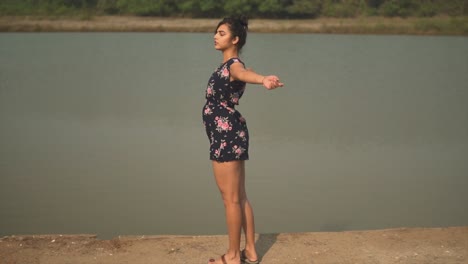 indian girl in a floral dress spinning in slowmotion with her arms wide open in front of a lake