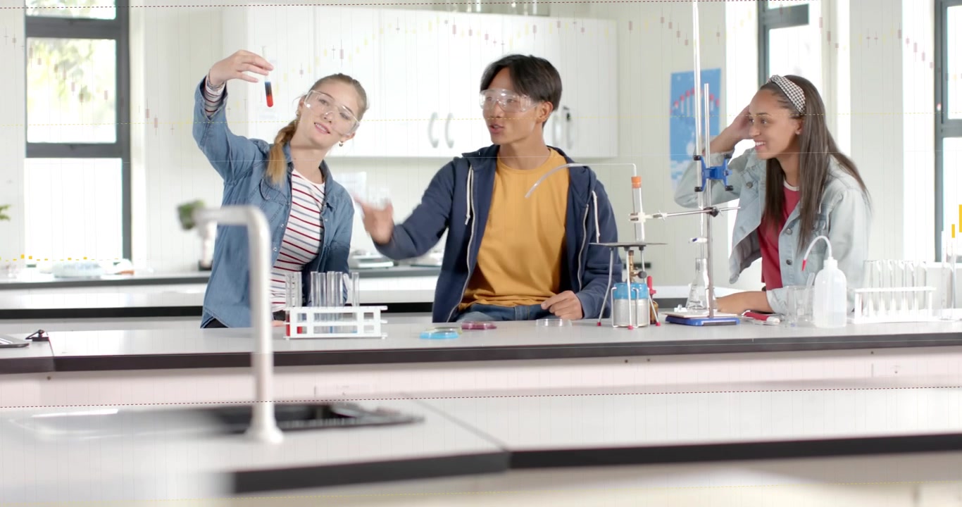 金髪の学生がバイアルとゴーグルを持ち、実験台に寄りかかって仲間とグラフで結果を確認している様子