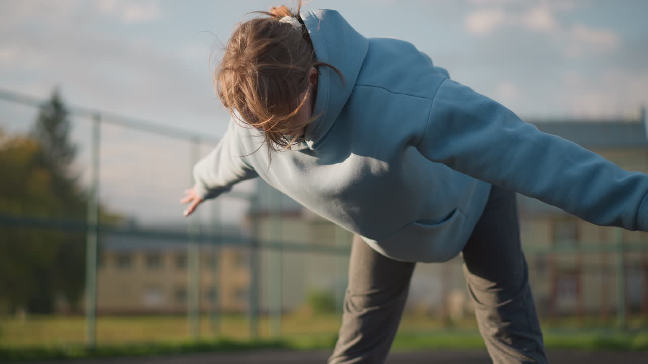 파란 스웨터를 입은 여자가 야외 코트에서 운동하고, 바람이 그녀의 머리카락을 들어 올릴 때 구부리고, 빛이 그녀의 움직임을 강조하며, 조용한 배경과 함께 역동적이고 활기찬 피트니스 순간을 만니다.