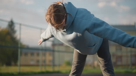 lady in blue sweater working out on outdoor court, bending as wind lifts her hair, sunlight highlights her movement, creating a dynamic and energetic fitness moment with a serene background