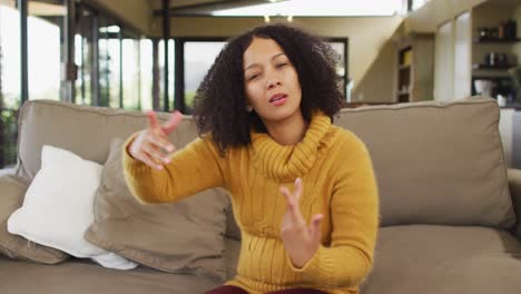 Happy-mixed-race-woman-sitting-on-couch-in-living-room,-talking-and-smiling-during-video-call