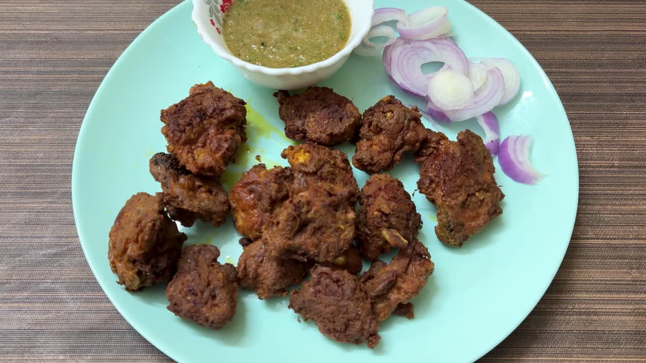 Rapea friteerattu kana-pakora tarjoillaan vihreän chutneyn ja sipuliviipaleiden kera.