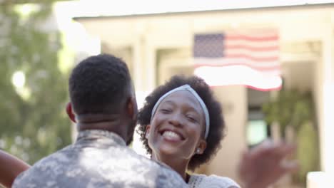 feliz soldado afroamericano abrazando a su esposa con bandera estadounidense, en cámara lenta