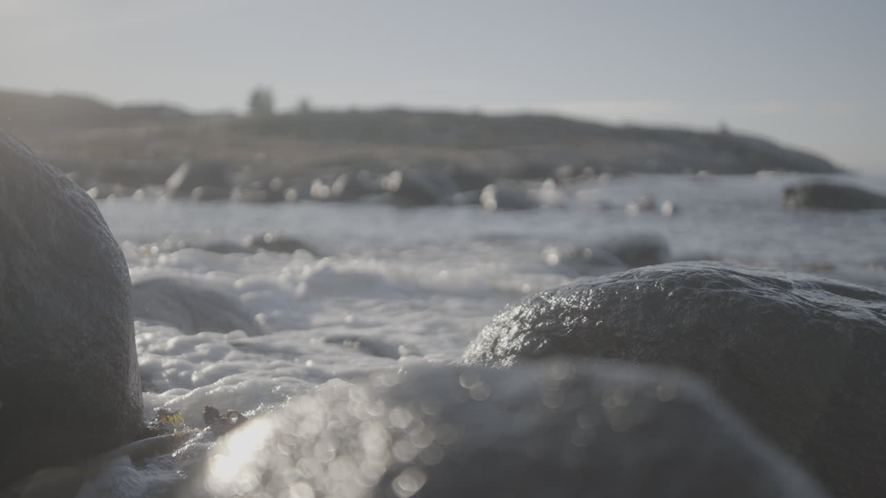 Water slowly clashing into the rocks with plants in between and focus shifting from foreground to the background near Brutt Lenke Norway on a sunny day LOG