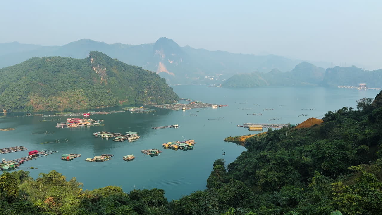 Wide view of floating houses and fish farms on a tranquil lake near Mộc Châu, Vietnam, surrounded by green hills. Ideal for nature, travel, or cultural visuals.