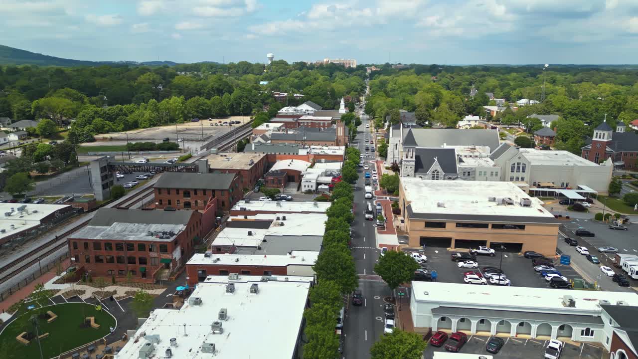 Aerial orbit shot of main street with cars in Marietta city. Wide shot. Church and historic buildings with green forest trees. Panorama view.